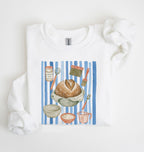 Flat lay of a white Sourdough baking tools sweatshirt featuring artisan bread, starter jar, banneton, and baking supplies on a white background 