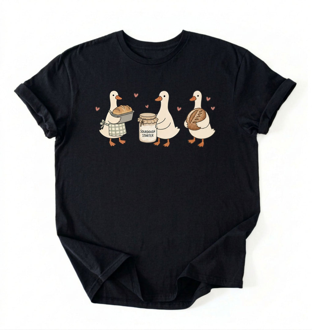 Flat lay of a black Cute sourdough ducks graphic shirt featuring bread and sourdough starter design for bakers on a white background