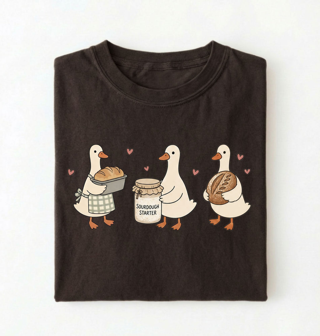 Flat lay of a Cute sourdough ducks graphic shirt featuring bread and sourdough starter design for bakers on a white background