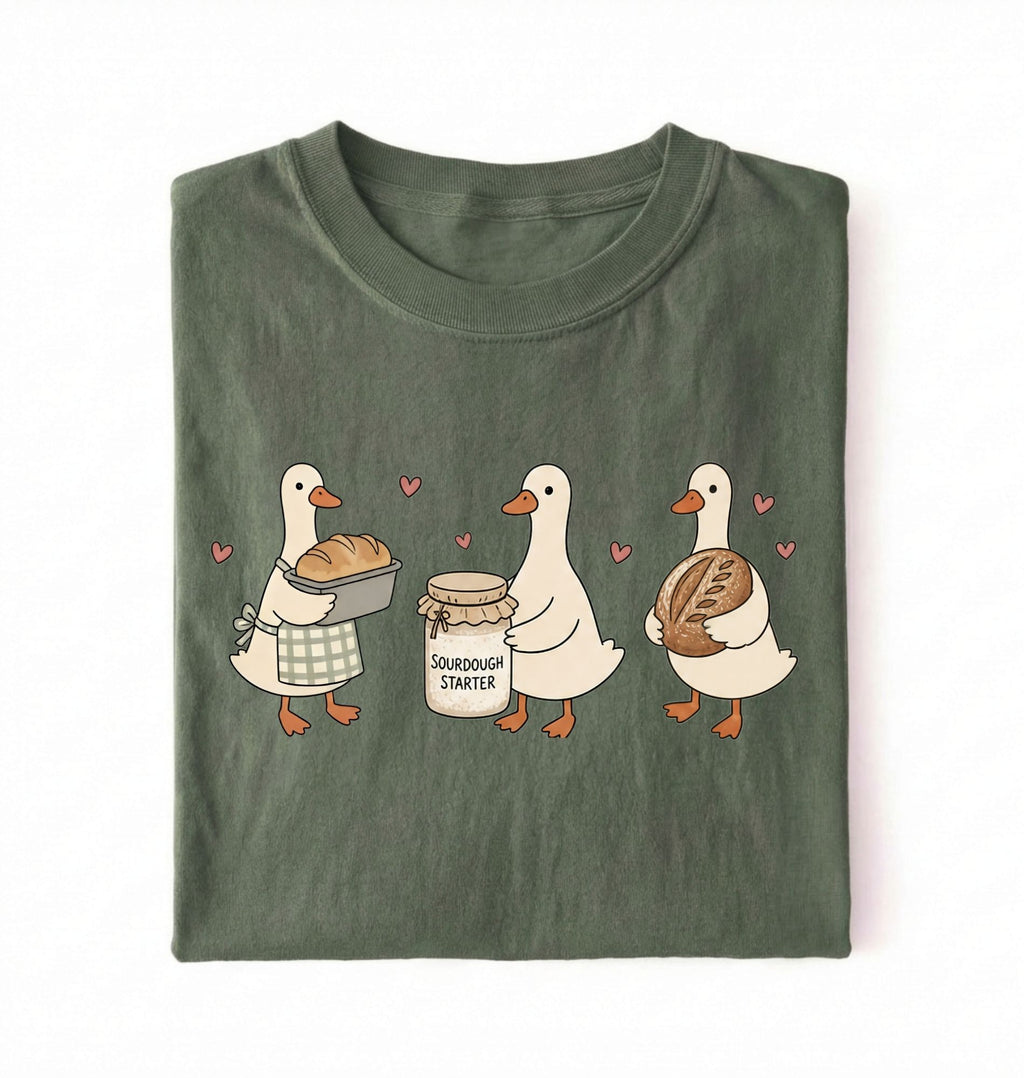 Flat lay of a green Cute sourdough ducks graphic shirt featuring bread and sourdough starter design for bakers on a white background