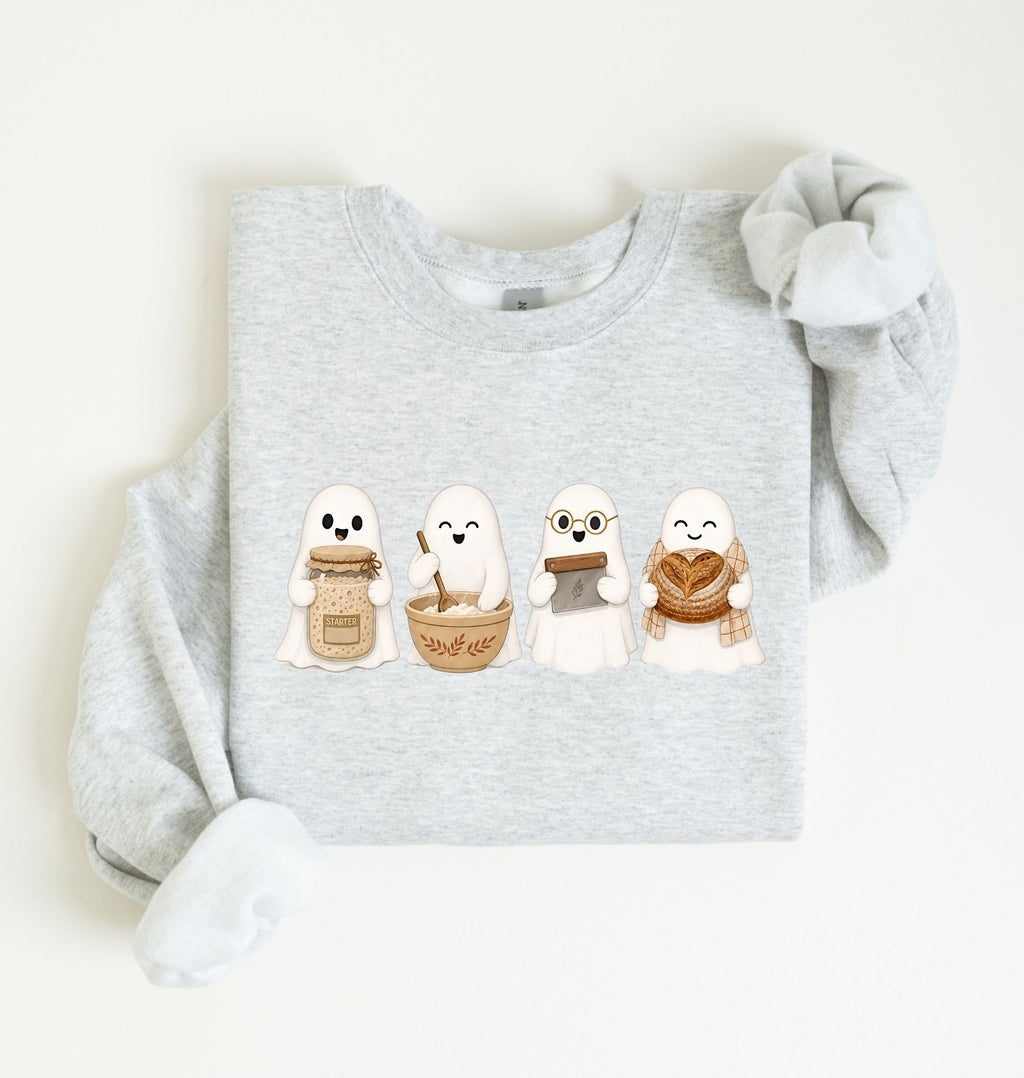 Flat lay of an ash sourdough sweatshirt featuring four cute baking ghosts with a starter jar, mixing bowl, bench scraper and bread loaf on a white background 