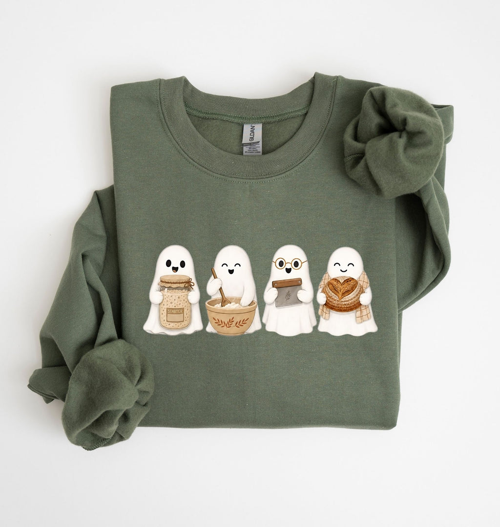 Flat lay of a green sourdough sweatshirt featuring four cute baking ghosts with a starter jar, mixing bowl, bench scraper and bread loaf on a white background 