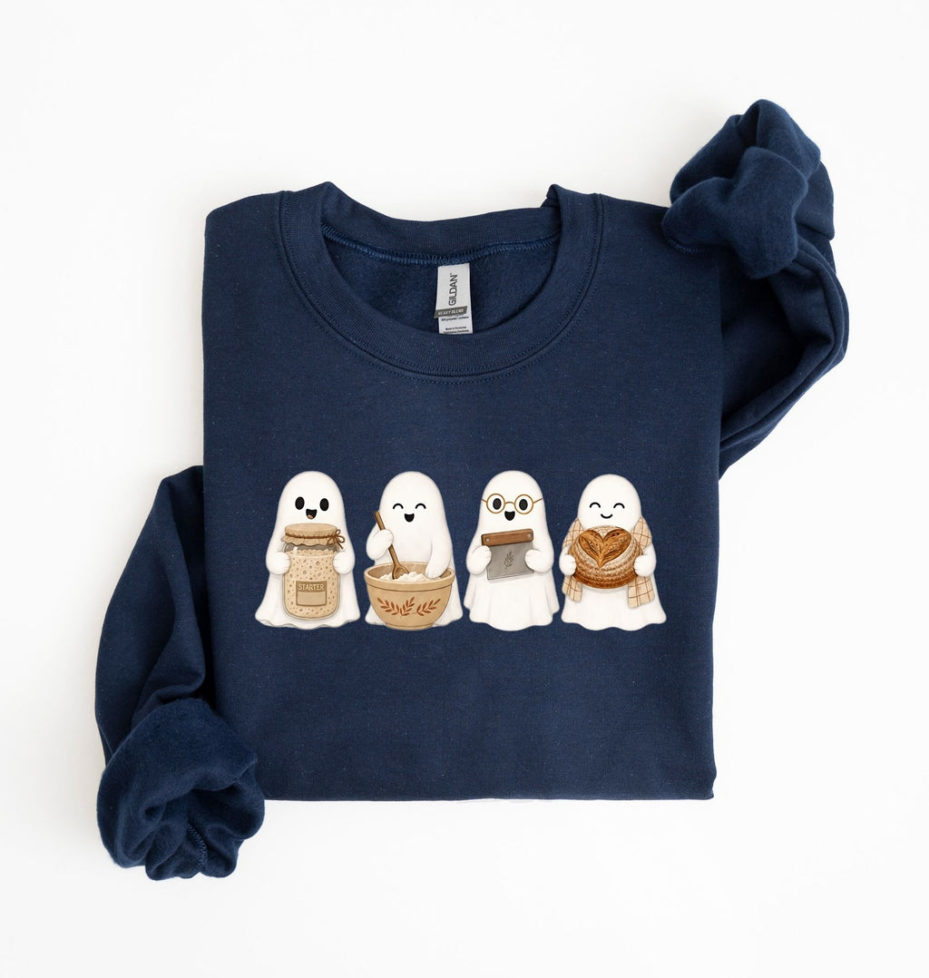 Flat lay of a navy sourdough sweatshirt featuring four cute baking ghosts with a starter jar, mixing bowl, bench scraper and bread loaf on a white background 