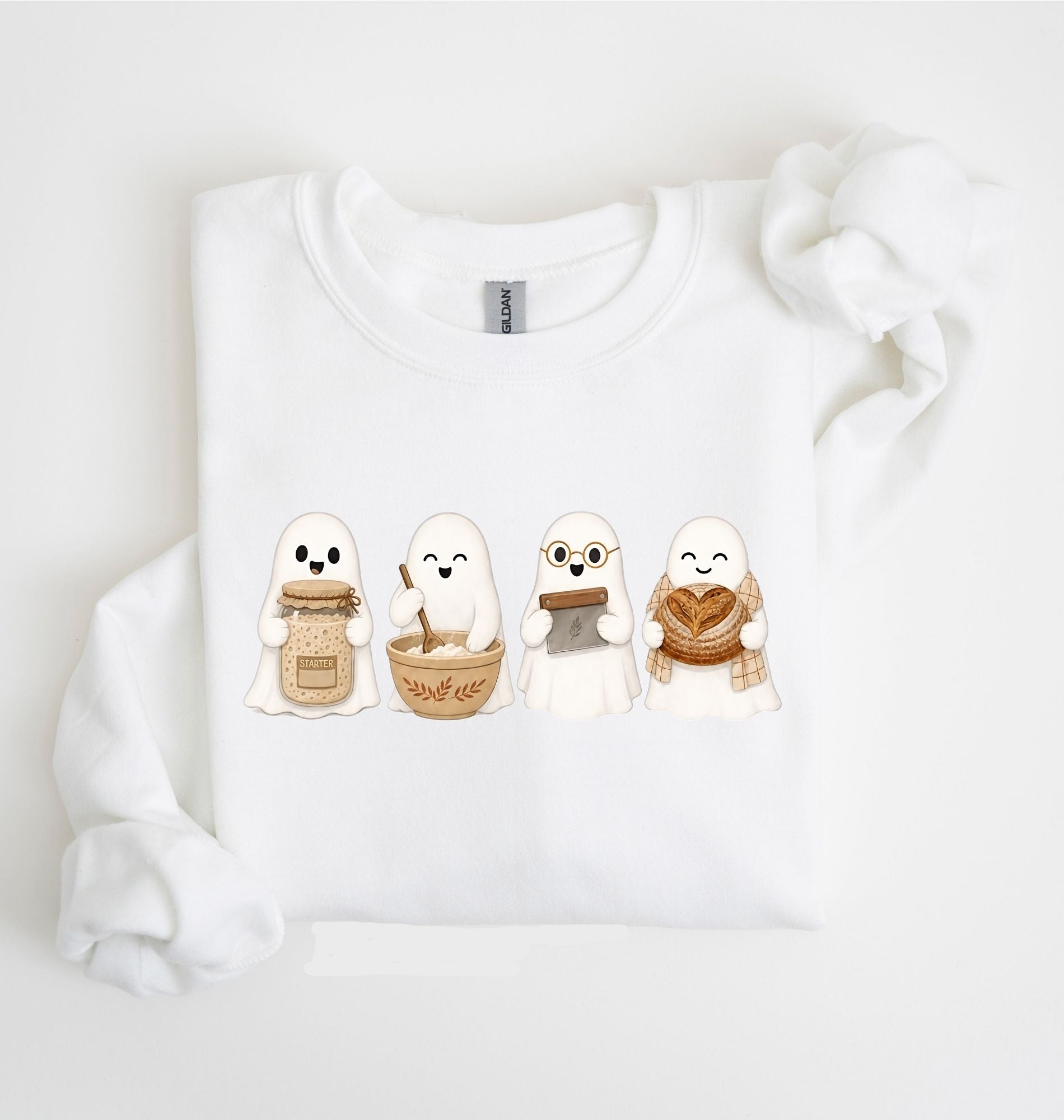 Flat lay of a white sourdough sweatshirt featuring four cute baking ghosts with a starter jar, mixing bowl, bench scraper and bread loaf on a white background 