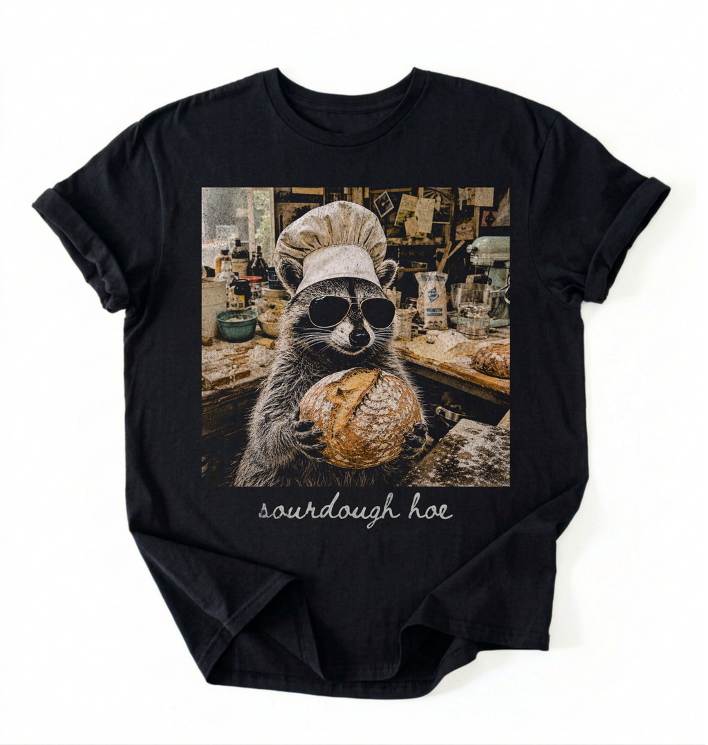 Flat lay of a sourdough hoe shirt black funny raccoon baker t shirt sourdough bread lover gift on a white background 