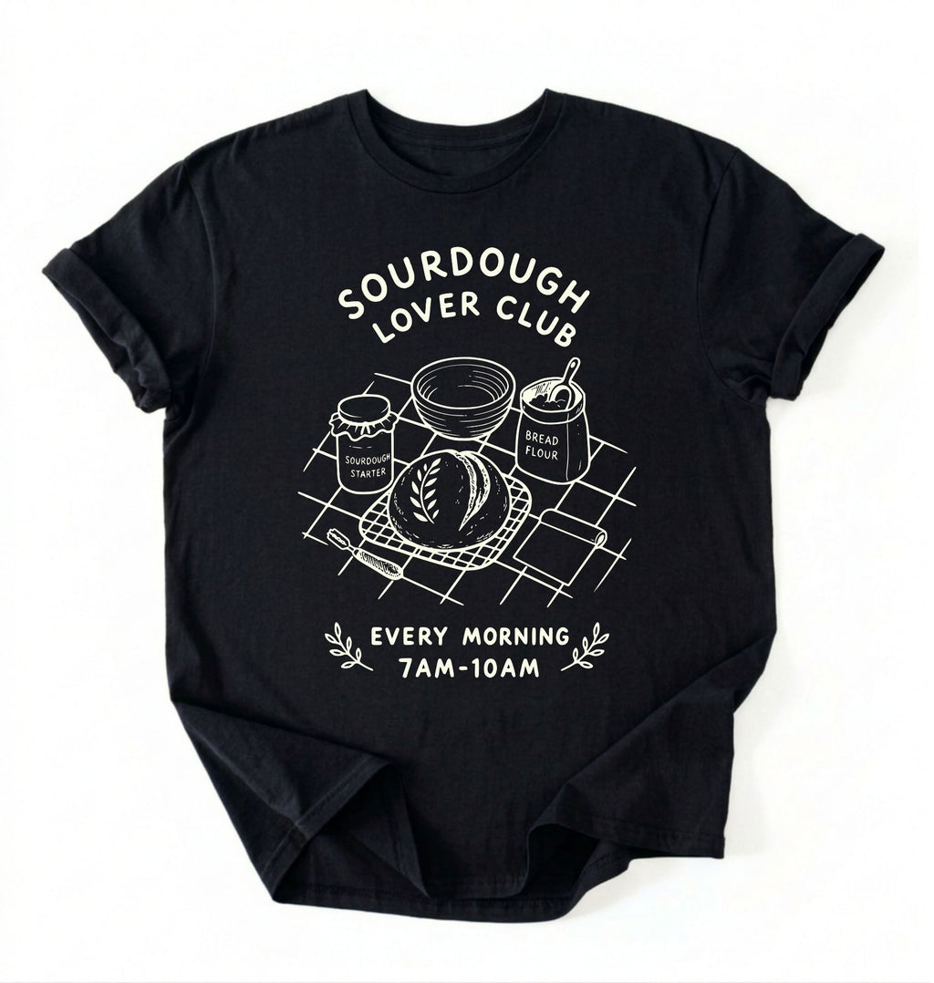 Flat lay of a black Sourdough Lover Club graphic shirt with artisan bread baking design for sourdough enthusiasts on a white background 