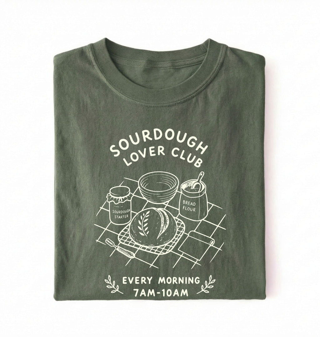 Flat lay of a green Sourdough Lover Club graphic shirt with artisan bread baking design for sourdough enthusiasts on a white background 