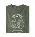Flat lay of a green Sourdough Lover Club graphic shirt with artisan bread baking design for sourdough enthusiasts on a white background 