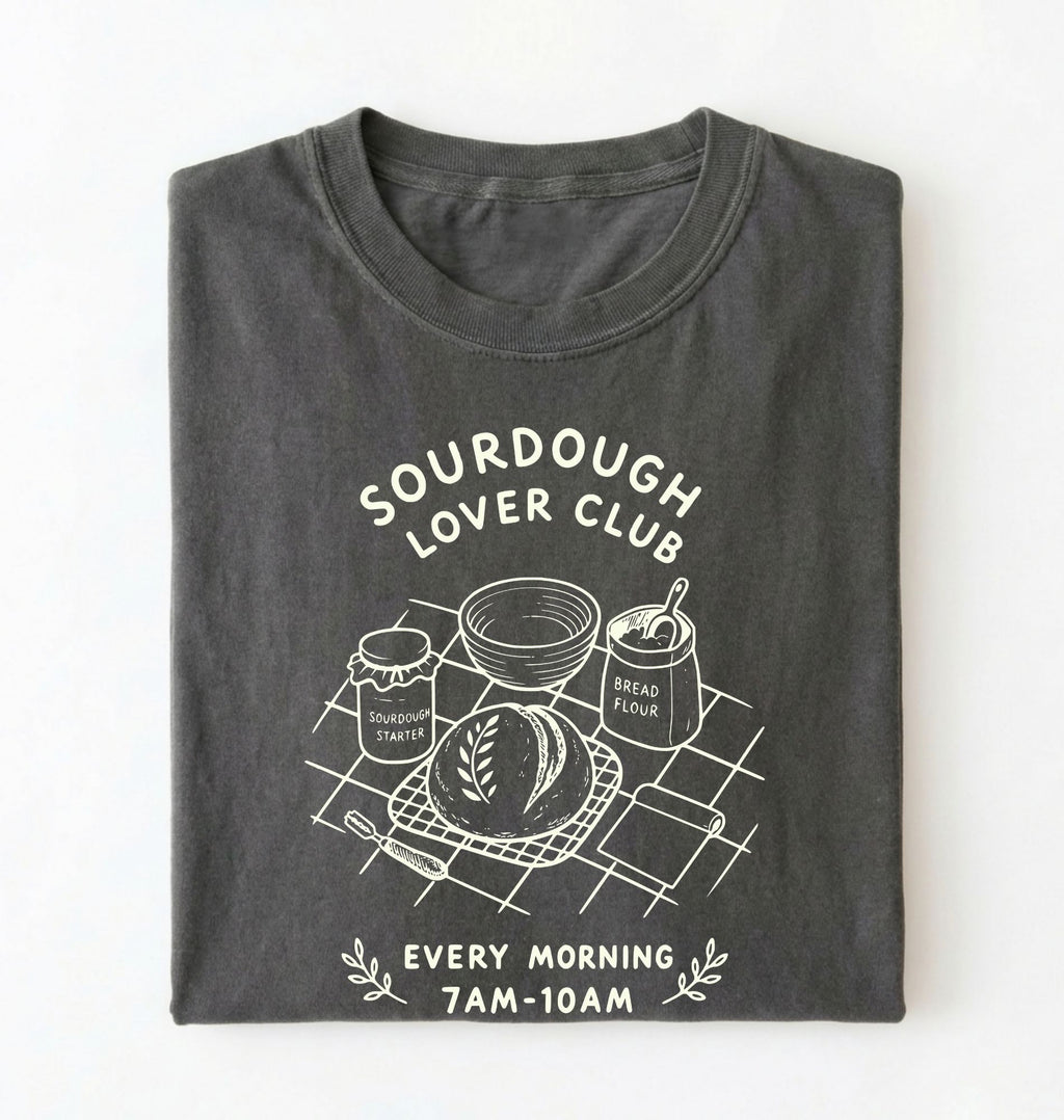 Flat lay of a gray Sourdough Lover Club graphic shirt with artisan bread baking design for sourdough enthusiasts on a white background 