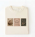 Flat lay of a cream sourdough mama shirt brown vintage baking stamps t shirt bread lover gift cozy kitchen design on a white background