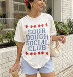 Woman wearing a 'Sour Dough Social Club' t-shirt outdoors.