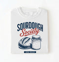 Flat lay of a white sourdough society shirt with artisan bread and sourdough starter jar for bread bakers on a white background 