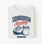 Flat lay of a white sourdough society shirt with artisan bread and sourdough starter jar for bread bakers on a white background 