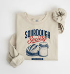 Flat lay of an sand Sourdough Society graphic sweatshirt with artisan bread and sourdough starter jar for bread bakers on a white background 
