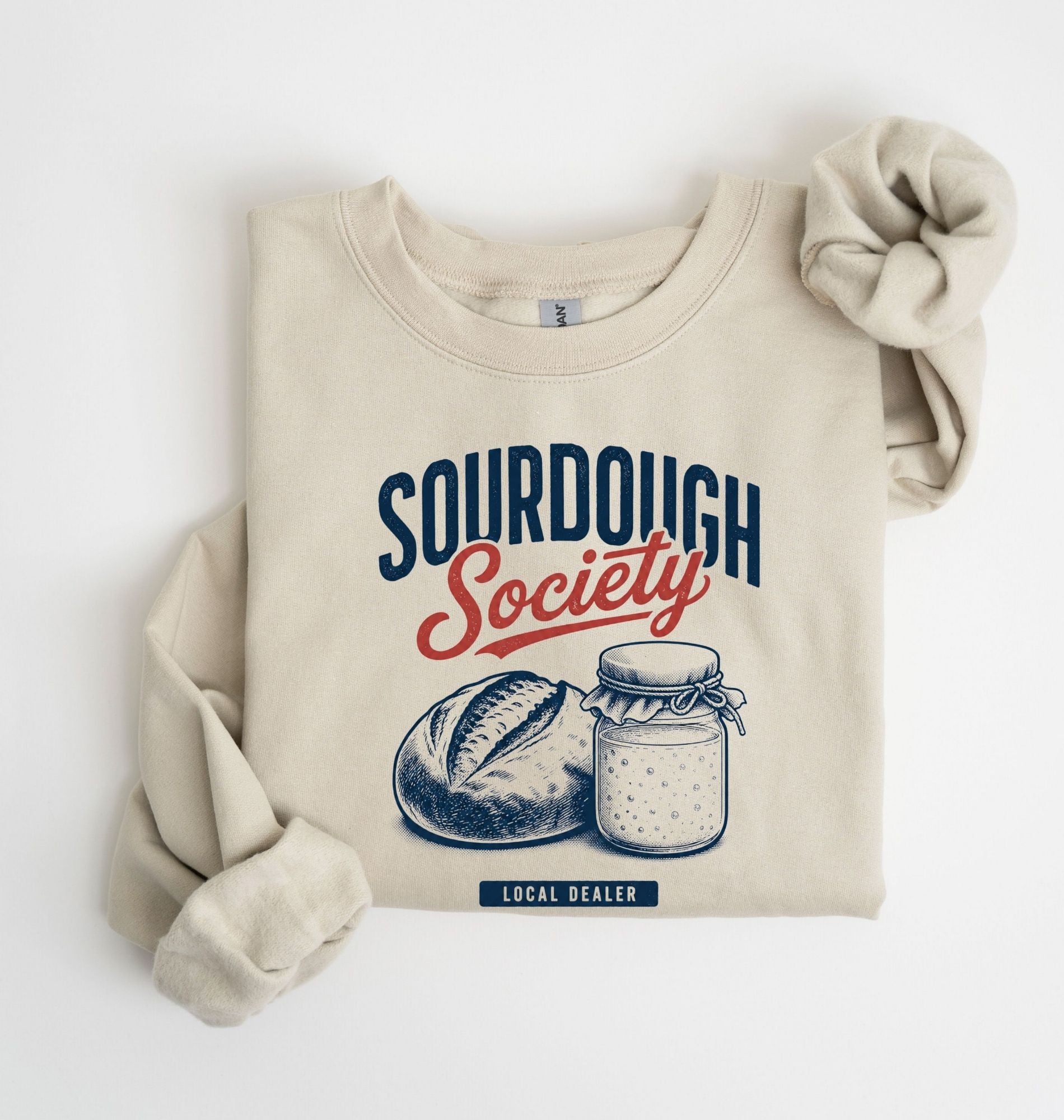 Flat lay of an sand Sourdough Society graphic sweatshirt with artisan bread and sourdough starter jar for bread bakers on a white background 