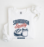 Flat lay of an white Sourdough Society graphic sweatshirt with artisan bread and sourdough starter jar for bread bakers on a white background 