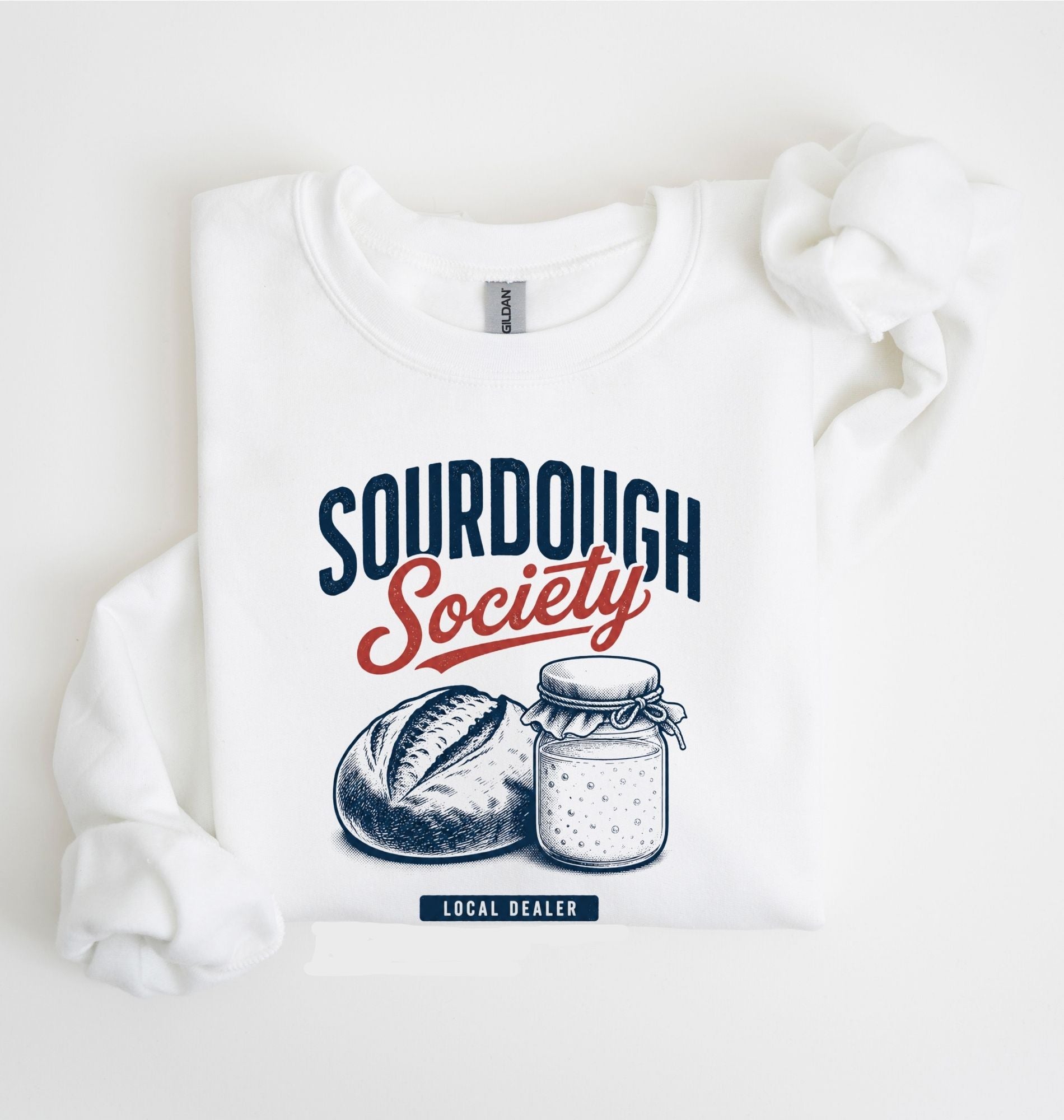 Flat lay of an white Sourdough Society graphic sweatshirt with artisan bread and sourdough starter jar for bread bakers on a white background 