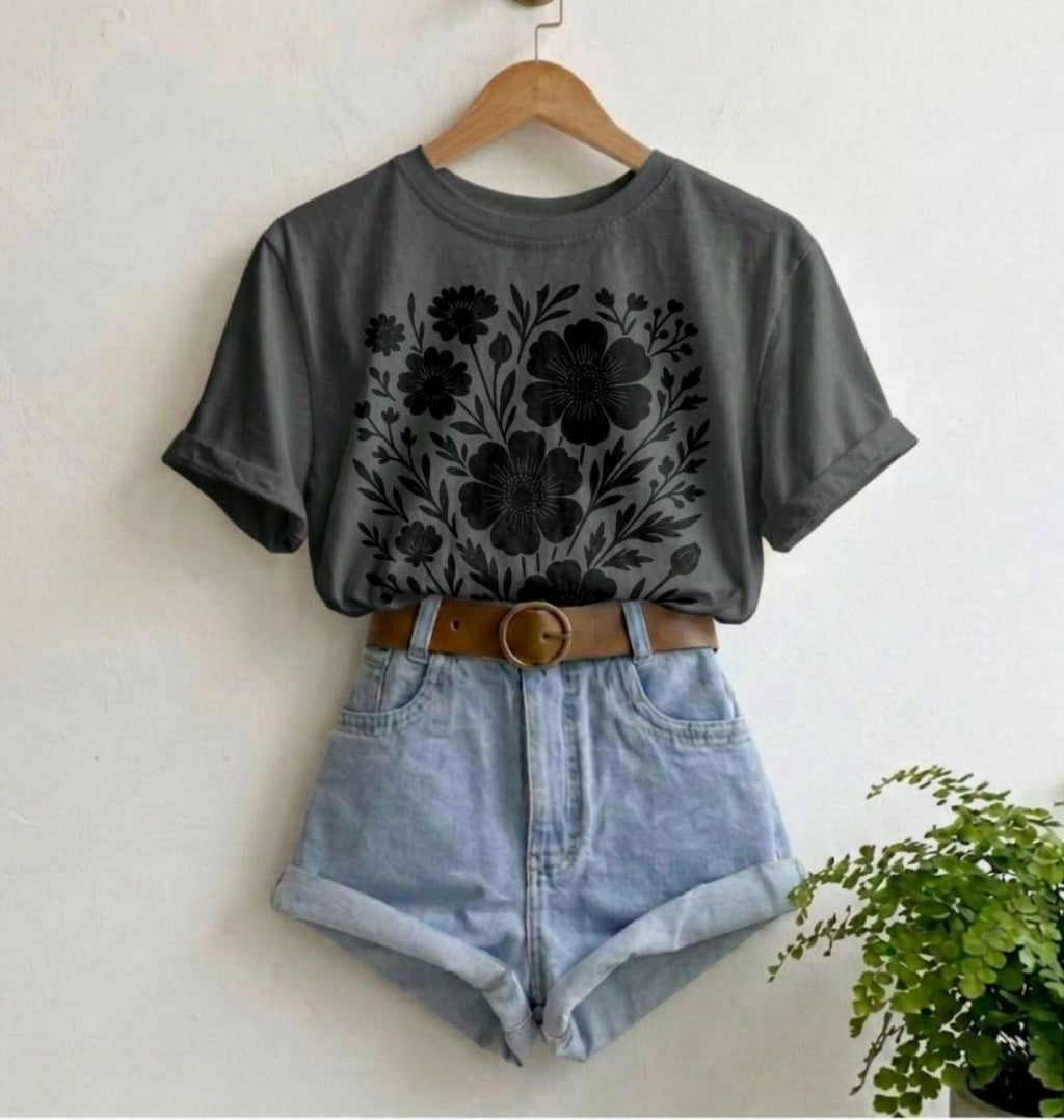 Gray t-shirt with floral design, denim shorts, and brown belt on a hanger against a white wall.