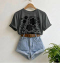 Gray t-shirt with floral design, denim shorts, and brown belt on a hanger against a white wall.