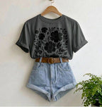 Gray t-shirt with floral design, denim shorts, and brown belt on a hanger against a white wall.