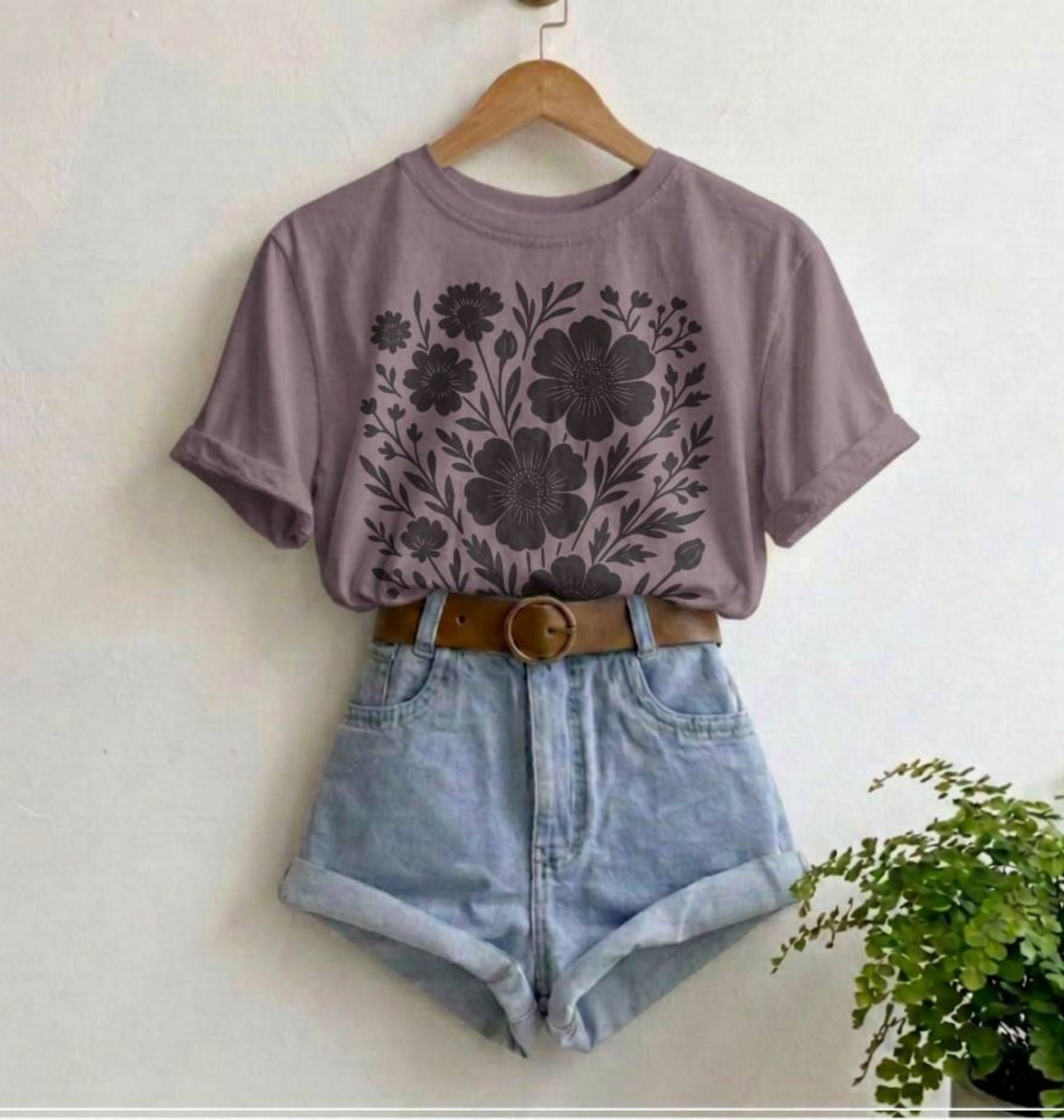Purple floral t-shirt and denim shorts on a hanger with a plant in the corner.