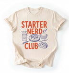 Flat lay of a cream starter nerd club shirt with sourdough starter jar bread and baking illustrations funny baker gift on a white background 