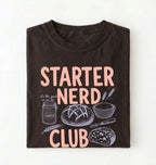 Flat lay of a brown starter nerd club shirt with sourdough starter jar bread and baking illustrations funny baker gift on a white background 