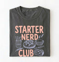 Flat lay of a pepper starter nerd club shirt with sourdough starter jar bread and baking illustrations funny baker gift on a white background 