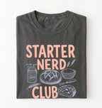 Flat lay of a pepper starter nerd club shirt with sourdough starter jar bread and baking illustrations funny baker gift on a white background 