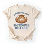 Flat lay of a Support Your Local Sourdough Dealer shirt with artisan sourdough bread graphic on ivory tee on a white background 