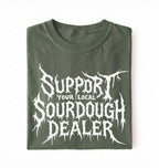 A folded dark olive green t-shirt with a white graphic print that reads 'SUPPORT YOUR LOCAL SOURDOUGH DEALER' in a stylized, dripping font, displayed against a plain white background.