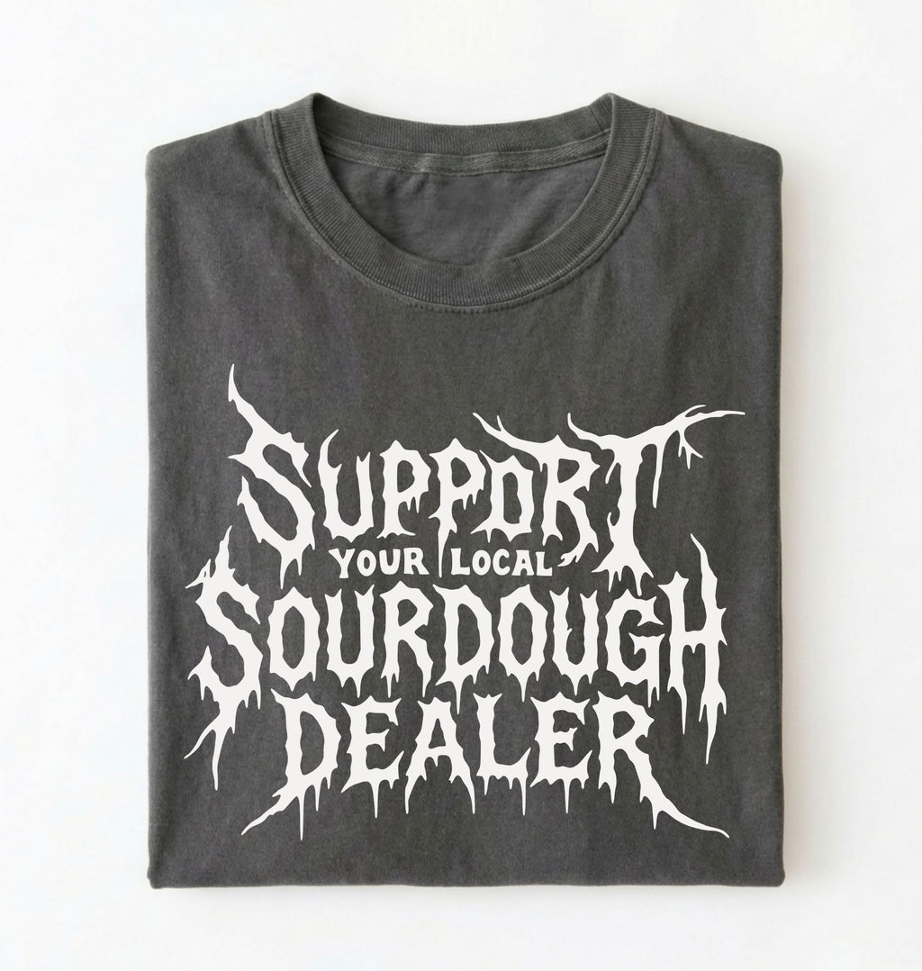 A folded dark gray t-shirt with a white distressed metal-style graphic reading 'SUPPORT YOUR LOCAL SOURDOUGH DEALER' on a plain white background.