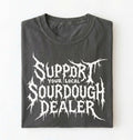 A folded dark gray t-shirt with a white distressed metal-style graphic reading 'SUPPORT YOUR LOCAL SOURDOUGH DEALER' on a plain white background.