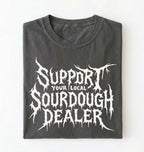 A folded dark gray t-shirt with a white distressed metal-style graphic reading 'SUPPORT YOUR LOCAL SOURDOUGH DEALER' on a plain white background.