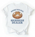 Flat lay of a Support Your Local Sourdough Dealer shirt with artisan sourdough bread graphic on white tee on a white background 