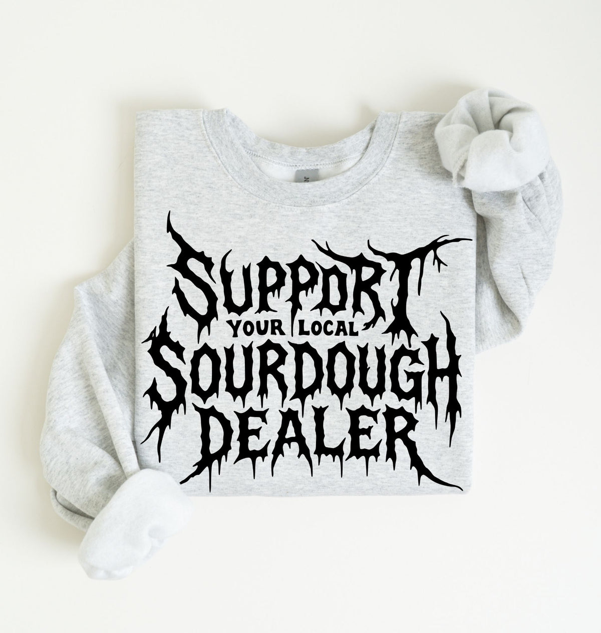 A light heather gray sweatshirt with a black graphic text reading 'SUPPORT YOUR LOCAL SOURDOUGH DEALER' in a stylized font, laid flat on a light cream background.