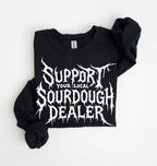 A black long-sleeve sweatshirt with rolled-up sleeves, featuring a white graphic text print that reads 'SUPPORT YOUR LOCAL SOURDOUGH DEALER' in a jagged, horror-style font. The sweatshirt is laid flat on a clean white background.