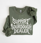 An olive green crewneck sweatshirt with rolled-up sleeves, featuring a white graphic print that reads 'SUPPORT YOUR LOCAL SOURDOUGH DEALER' in a stylized font, laid flat on a white background.
