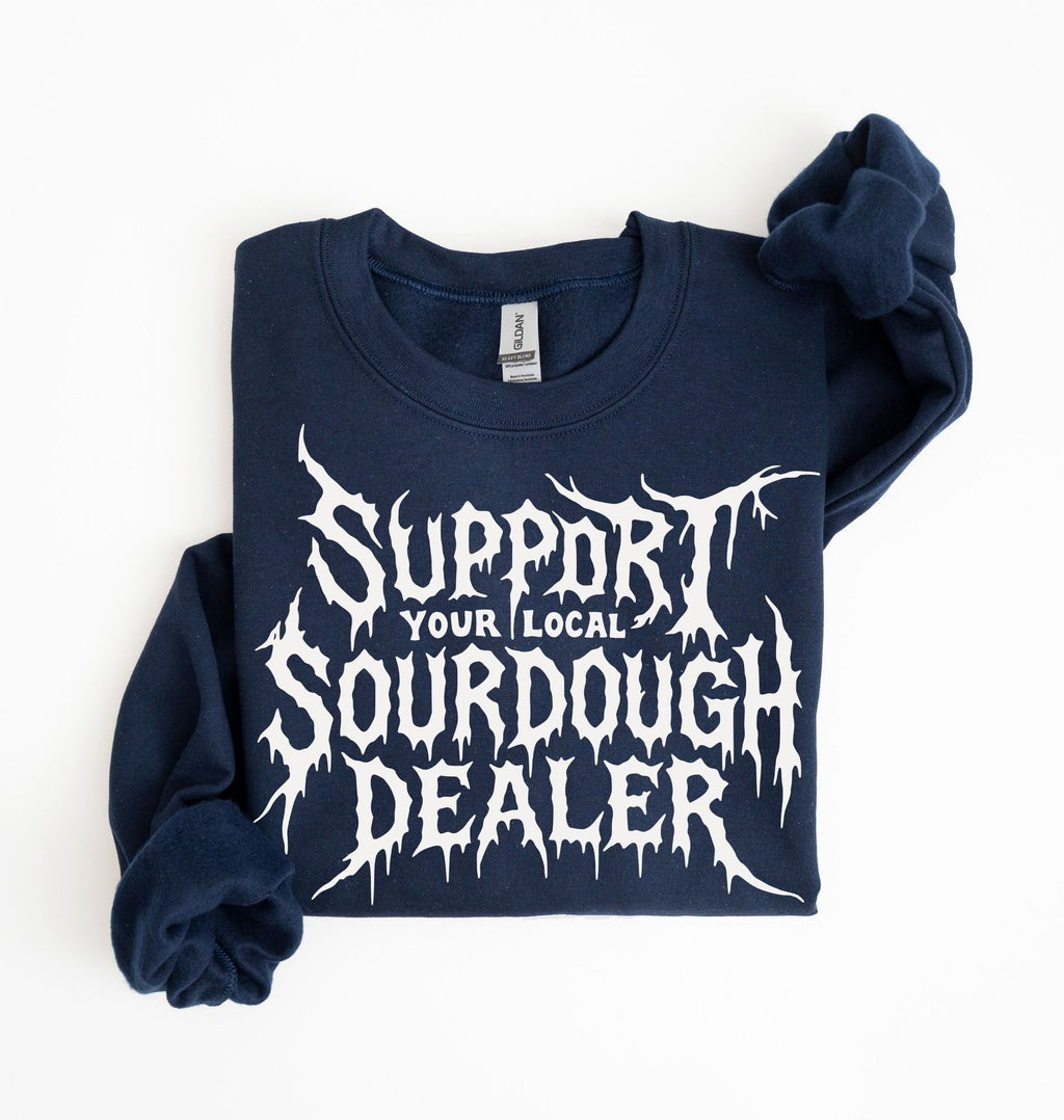 A navy blue sweatshirt with a white graphic print reading 'SUPPORT YOUR LOCAL SOURDOUGH DEALER' in a stylized font, folded neatly on a white background.