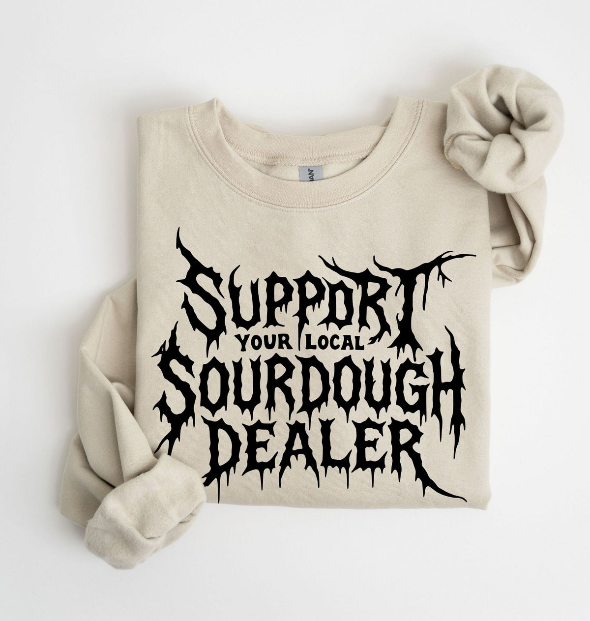 A folded beige crewneck sweatshirt with rolled sleeves, featuring a black graphic text print that reads 'SUPPORT YOUR LOCAL SOURDOUGH DEALER'.