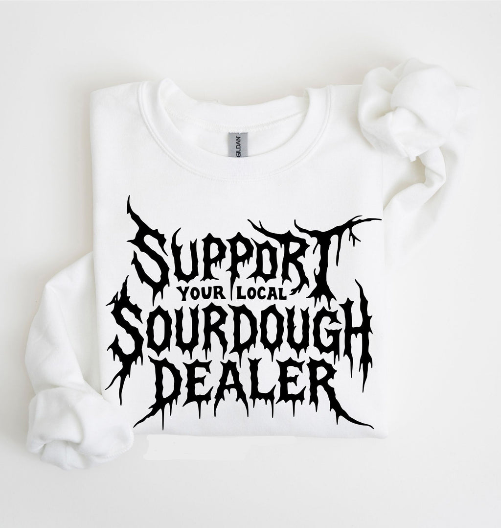 A white long-sleeve sweatshirt laid flat on a white background, featuring a large black distressed graphic that reads 'SUPPORT YOUR LOCAL SOURDOUGH DEALER' across the front.