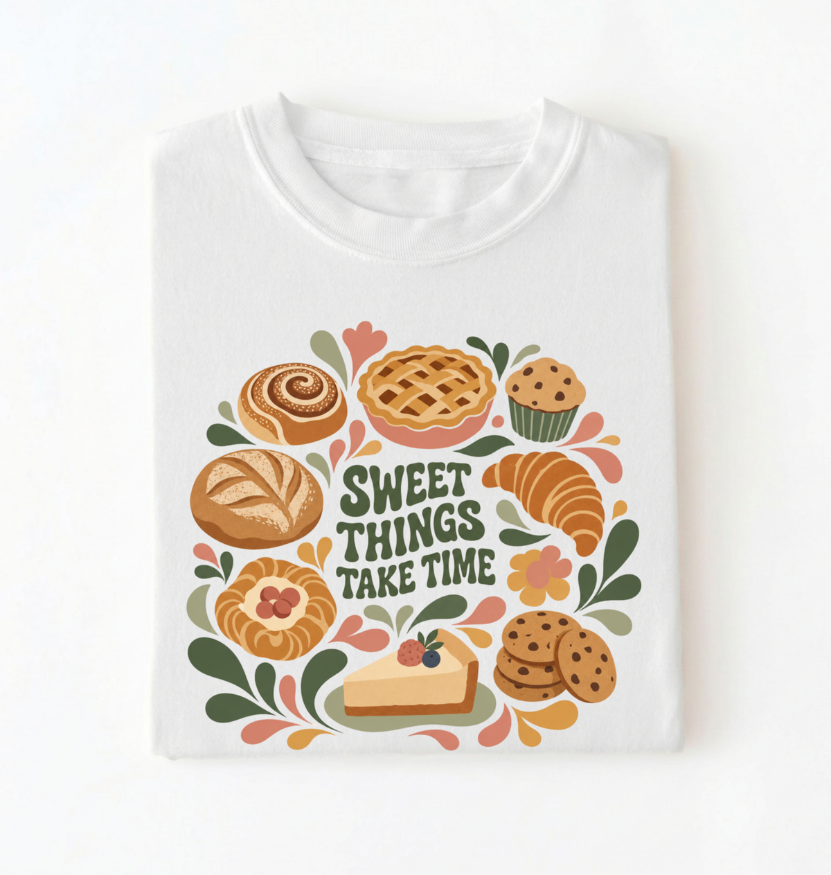 A white crewneck t-shirt with a colorful graphic print featuring various baked goods like a cinnamon roll, apple pie, croissant, muffin, and cookies surrounding the text 'SWEET THINGS TAKE TIME' in a retro font.