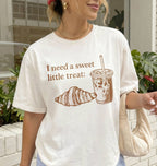 Person wearing a white t-shirt with a graphic and text 'I need a sweet little treat'.