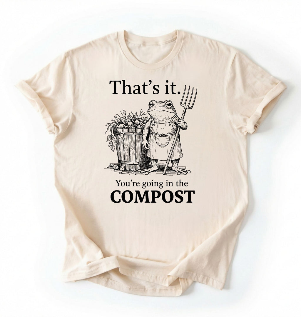 Flat lay of a Natural t-shirt featuring an illustrated frog with text reading “That’s it you’re going in the compost frog t-shirt” on a white background