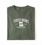Flat lay of a green Tired Moms Baking Club graphic shirt with stand mixer design for baking moms on a white background 