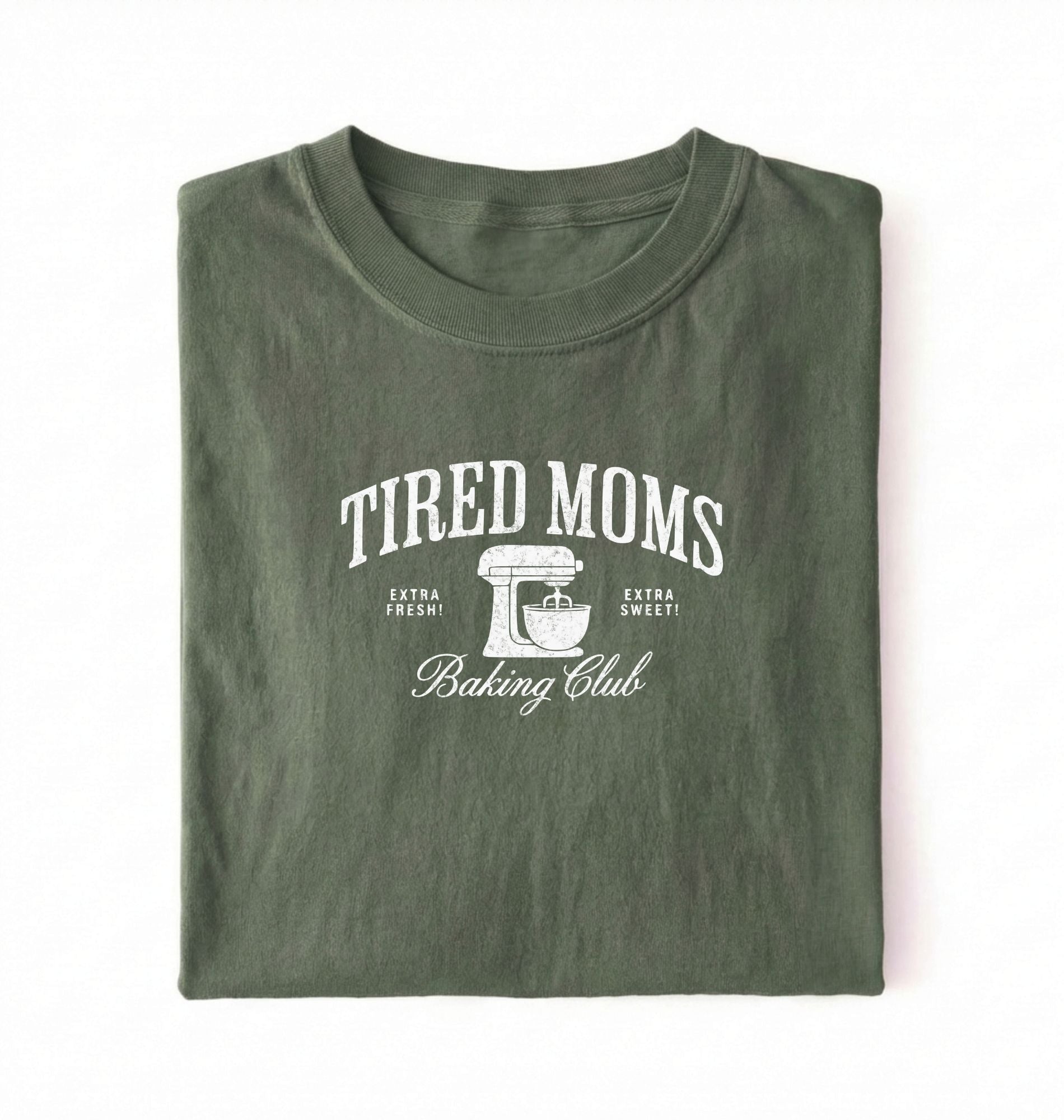 Flat lay of a green Tired Moms Baking Club graphic shirt with stand mixer design for baking moms on a white background 