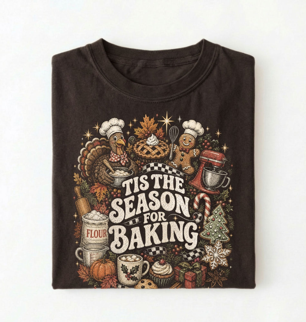 A folded dark brown t-shirt with a detailed graphic print featuring Thanksgiving baking elements like a turkey, pie, gingerbread man, stand mixer, and the text 'TIS THE SEASON FOR BAKING' on a white background.