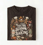 A folded dark brown t-shirt with a detailed graphic print featuring Thanksgiving baking elements like a turkey, pie, gingerbread man, stand mixer, and the text 'TIS THE SEASON FOR BAKING' on a white background.