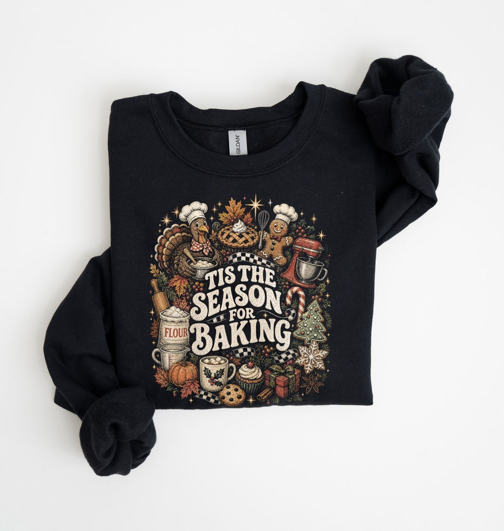 A black crewneck sweatshirt with rolled sleeves, featuring a colorful 'Tis the Season for Baking' graphic on the front, laid flat on a white background.