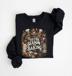 A black crewneck sweatshirt with rolled sleeves, featuring a colorful 'Tis the Season for Baking' graphic on the front, laid flat on a white background.